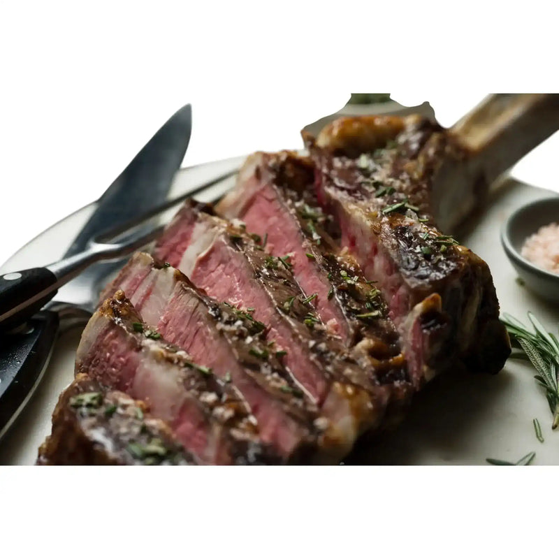 Sliced Diamantina Angus Tomahawk steak with herbs, gourmet salt, and cutlery on a plate, premium Australian beef from Peter Augustus