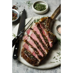 Sliced Angus tomahawk steak on a plate with herbs, knife and fork, pink and juicy center
