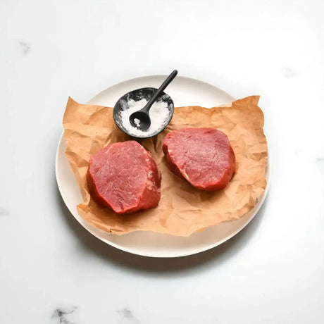 Two raw Diamantina grain-fed eye fillet steaks on parchment with a bowl of salt