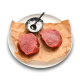 Two fresh raw beef steaks on parchment paper with salt, ready for cooking