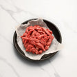 Raw stir fry beef strips on parchment paper in a black bowl, on a white marble surface
