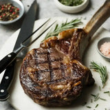 Grilled tomahawk steak on marble board with rosemary, salt, and pepper.