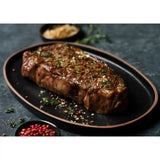 Grilled Diamantina Wagyu Picanha steak on a black plate with herbs and peppercorns