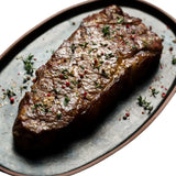 Grilled Wagyu sirloin steak garnished with herbs and pepper on a serving plate