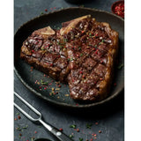 Cooked Diamantina T-bone steak garnished with herbs and peppercorns in a cast iron pan
