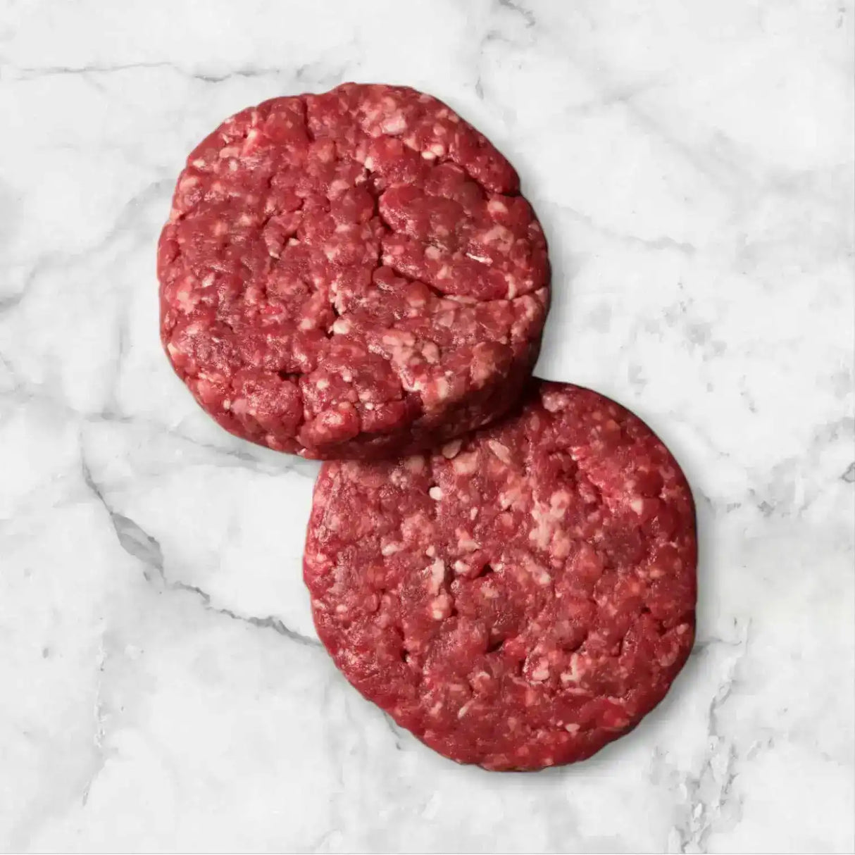 Two raw Diamantina Wagyu beef burger patties on a white marble surface