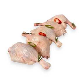 Two raw duck legs with red peppers and green herbs