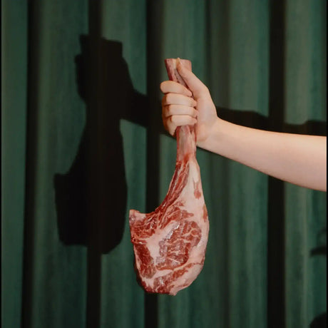 Hand holding premium marbled tomahawk steak from Peter Augustus Craft Butcher
