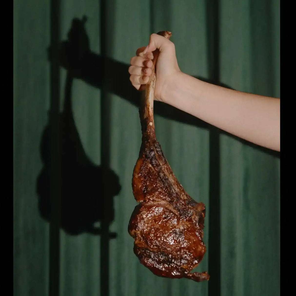 Hand holding cooked tomahawk steak from Peter Augustus Craft Butcher against green background
