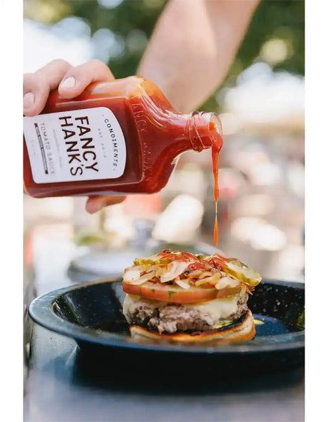 Pouring tomato sauce on a gourmet beef burger with cheese, tomato, pickles, and onions