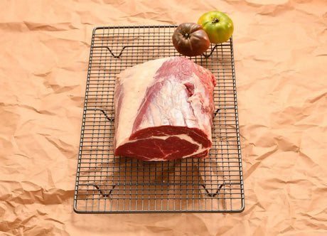 Raw rib fillet beef cut on wire rack with two heirloom tomatoes on butcher paper