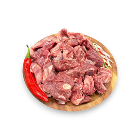 Fresh raw beef chunks on wooden board with red chili and herbs, ideal for stew or braising