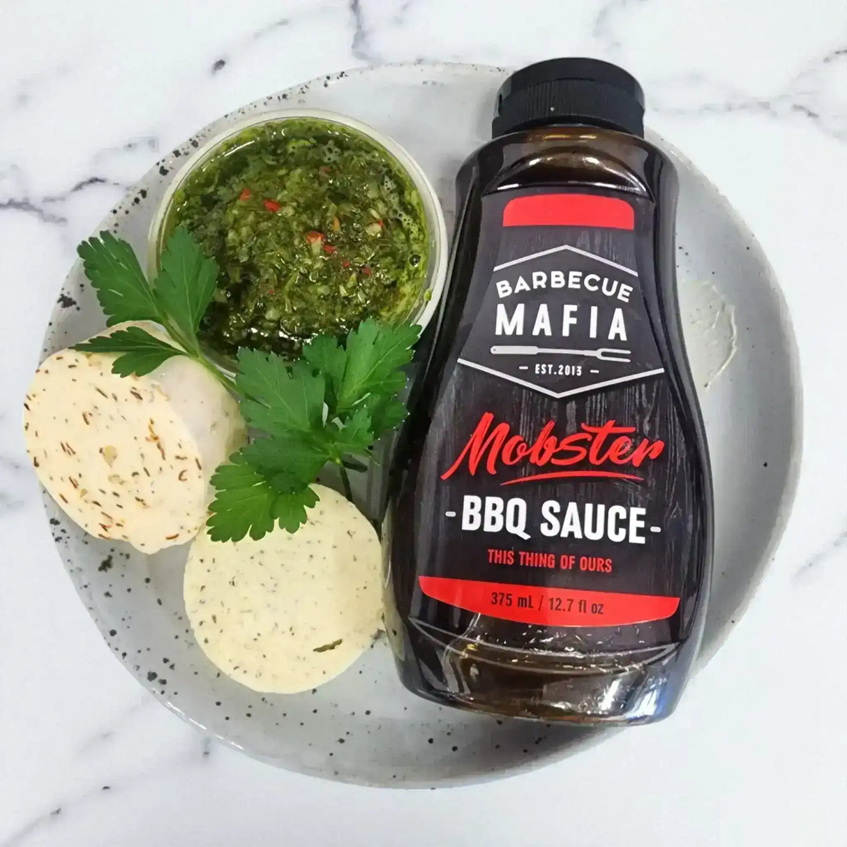BBQ sauce bottle, chimichurri, and compound butter rounds on a plate, gourmet condiments