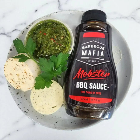BBQ sauce bottle, chimichurri, and compound butter rounds on a plate, gourmet condiments
