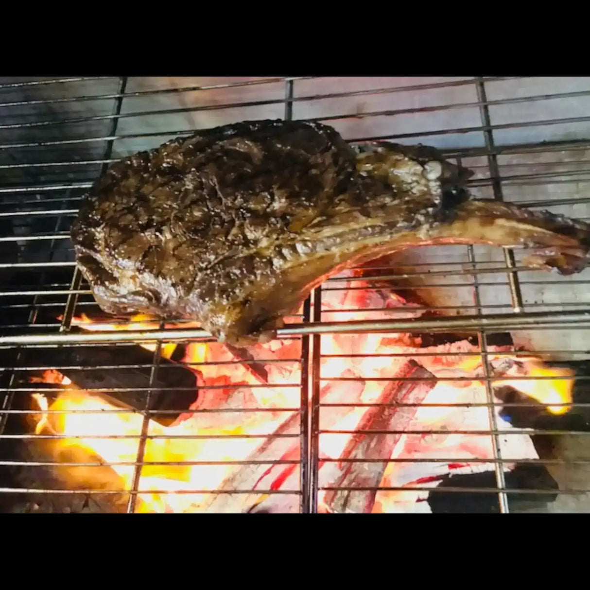 Australian bone-in ribeye steak grilling over open flames from Peter Augustus Craft Butcher
