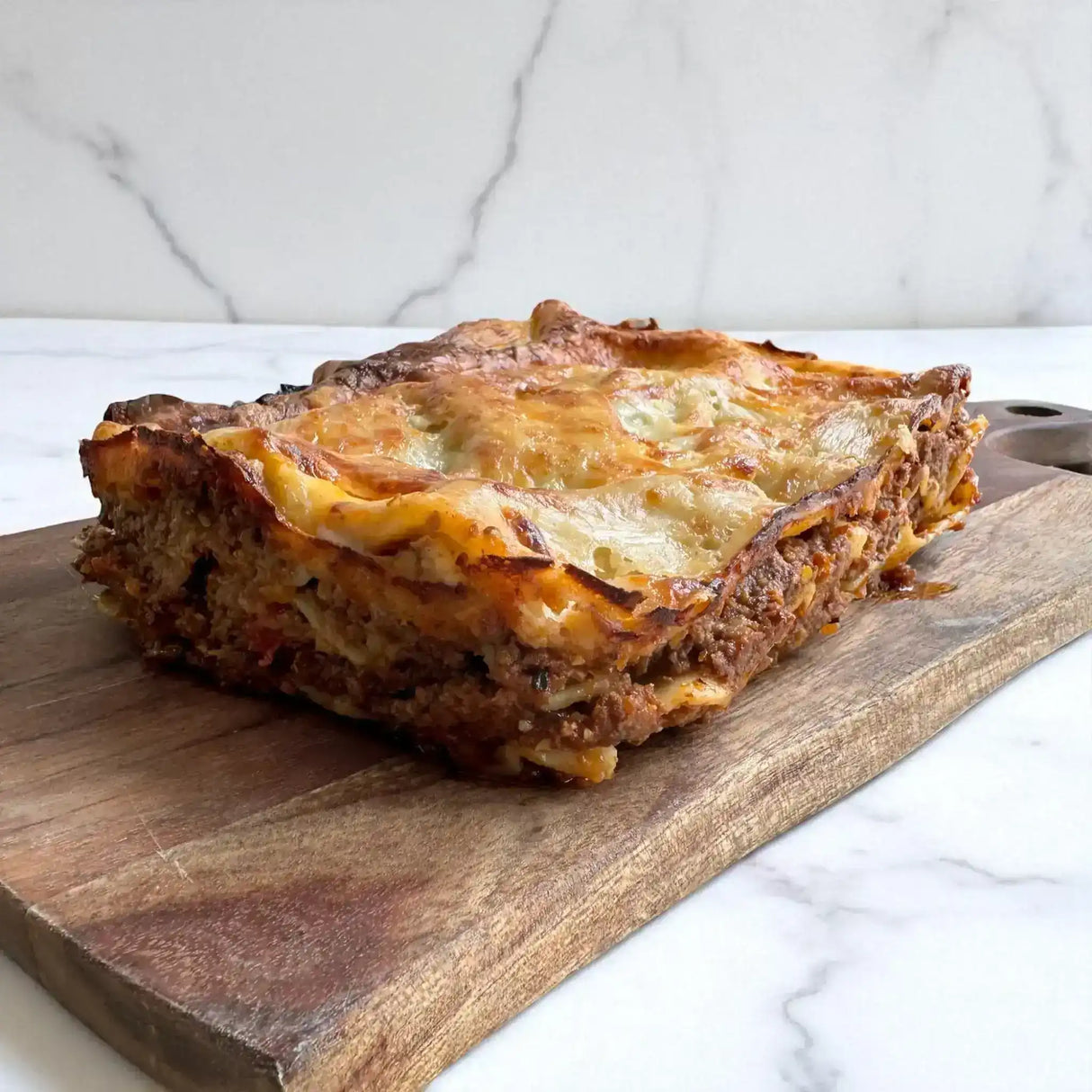 Australian beef lasagna with golden cheese crust on wooden board from Peter Augustus