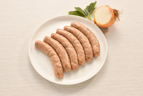 Six raw Irish pork sausages on a plate beside fresh sage and a halved onion