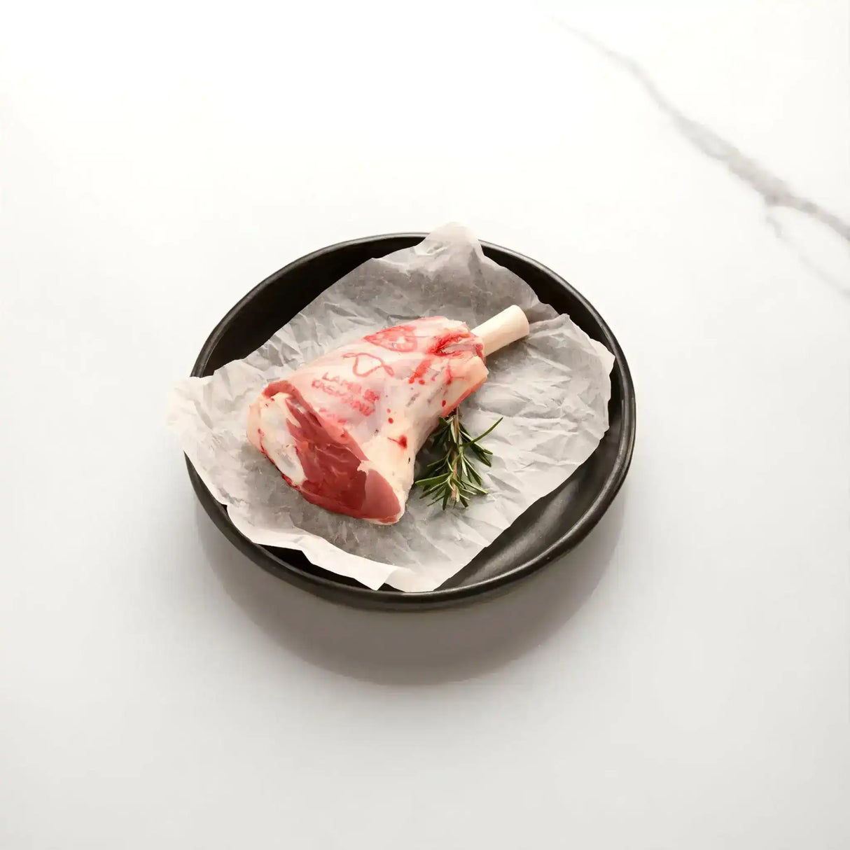 Raw lamb shank with rosemary on parchment in a black dish, Peter Augustus Craft Butcher