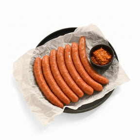 Raw lamb merguez sausages on parchment-lined plate with a side of spicy red relish