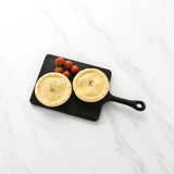 Two uncooked lamb shank and sweet potato pies with cherry tomatoes on a black serving board