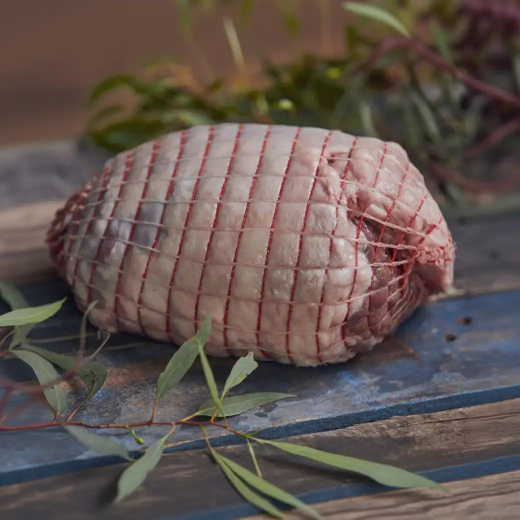 Rolled raw lamb on a rustic wooden surface with greenery