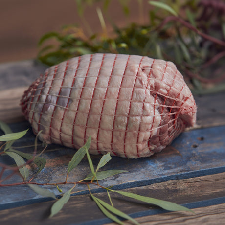 Rolled raw lamb on a rustic wooden surface with greenery