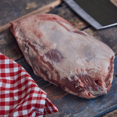 Raw Lamb shoulder meat on a wooden cutting board with a knife and checkered cloth.