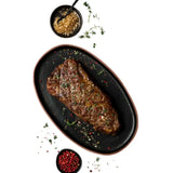 Cooked Australian Wagyu steak on black plate with herbs, salt, and peppercorns