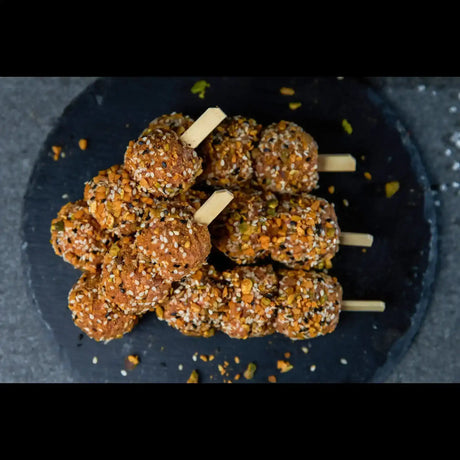 Seasoned meat skewers topped with herbs and sesame seeds on a dark slate serving platter