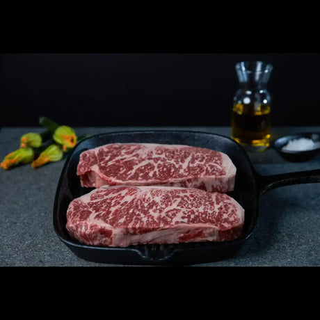 Premium marbled Wagyu steaks from Peter Augustus in a pan, with oil and salt nearby