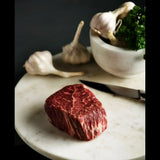 Raw Wagyu eye fillet steak with marbling on a marble board, garlic, herbs, and knife