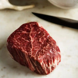 Raw Wagyu eye fillet steak on marble board with visible marbling, garlic, and knife nearby.