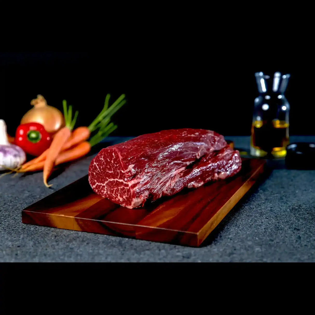Raw Wagyu eye fillet steak on wooden board with vegetables and oil in background