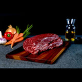 Raw Wagyu eye fillet steak on wooden board with vegetables and oil in background