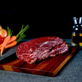 Raw Wagyu eye fillet steak on wooden board with carrots, onion, and oil in the background