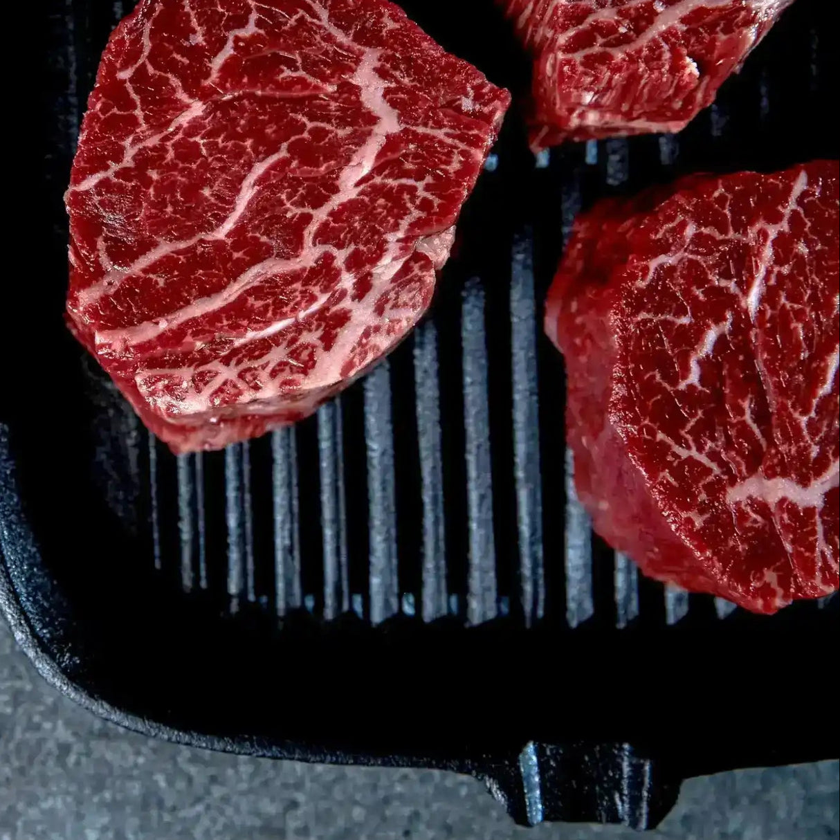 Raw Wagyu eye fillet steaks with rich marbling on a grill pan, peppercorns on the side