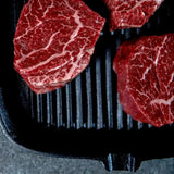 Raw Wagyu eye fillet steaks with rich marbling on a grill pan, peppercorns on the side