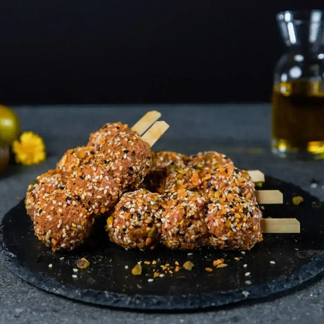 Raw seasoned Lamb skewers with sesame seeds on a black slate, gourmet butcher display