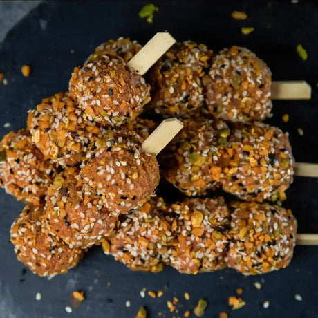 Seasoned lamb meat skewers topped with herbs and sesame seeds on a dark slate serving platter