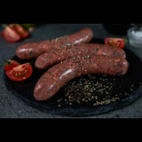 Raw gourmet beef sausages with cracked pepper and tomato slices on a slate board