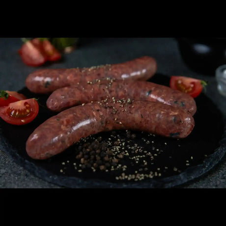 Peter Augustus gourmet beef sausages with pepper and fresh tomato slices on a black plate