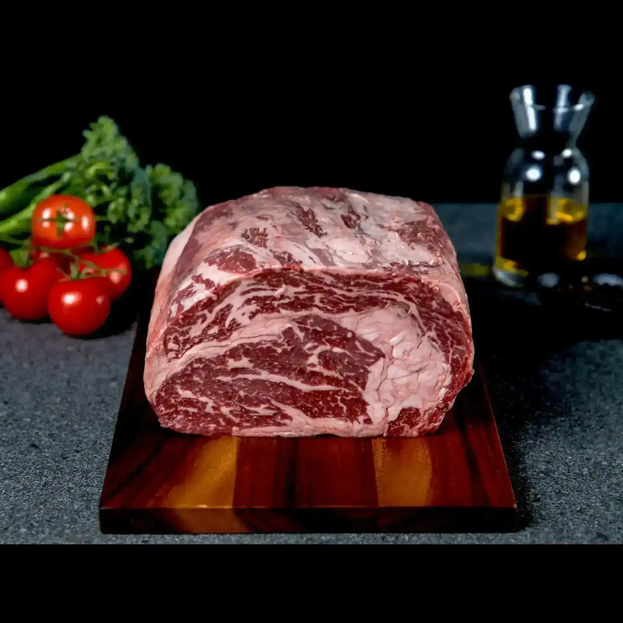 Premium marbled beef roast from Peter Augustus Craft Butcher on a wooden board, fresh tomatoes and greens nearby.