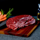 Raw Wagyu tenderloin beef with rich marbling on a wooden board, vegetables in background