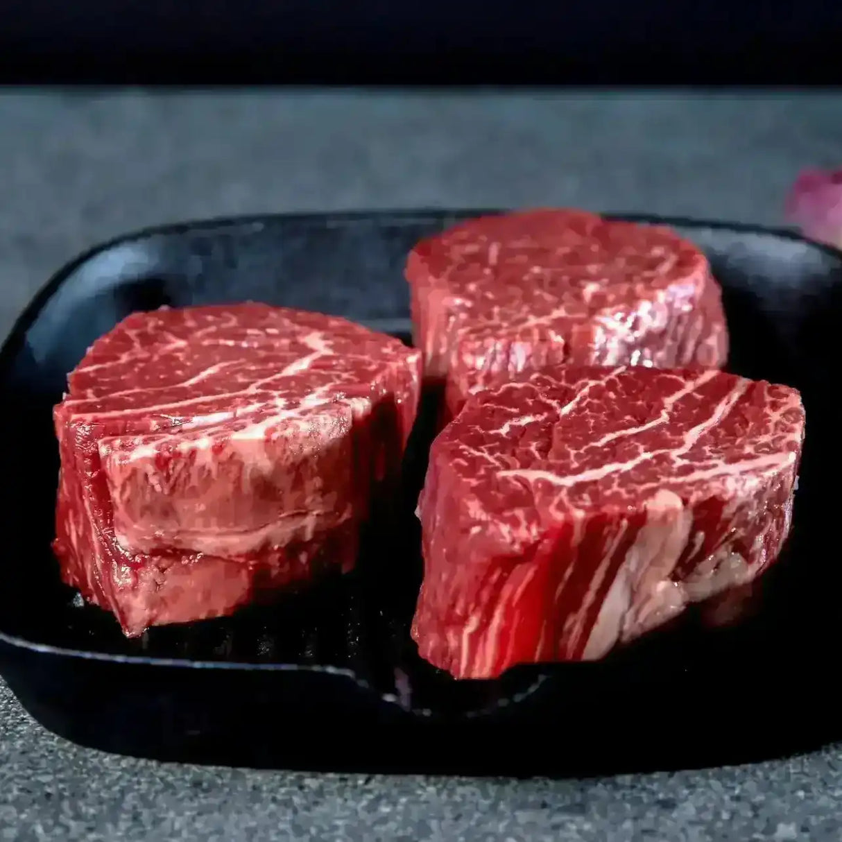 Raw Wagyu tenderloin eye fillet steaks with marbling on a dark grill pan