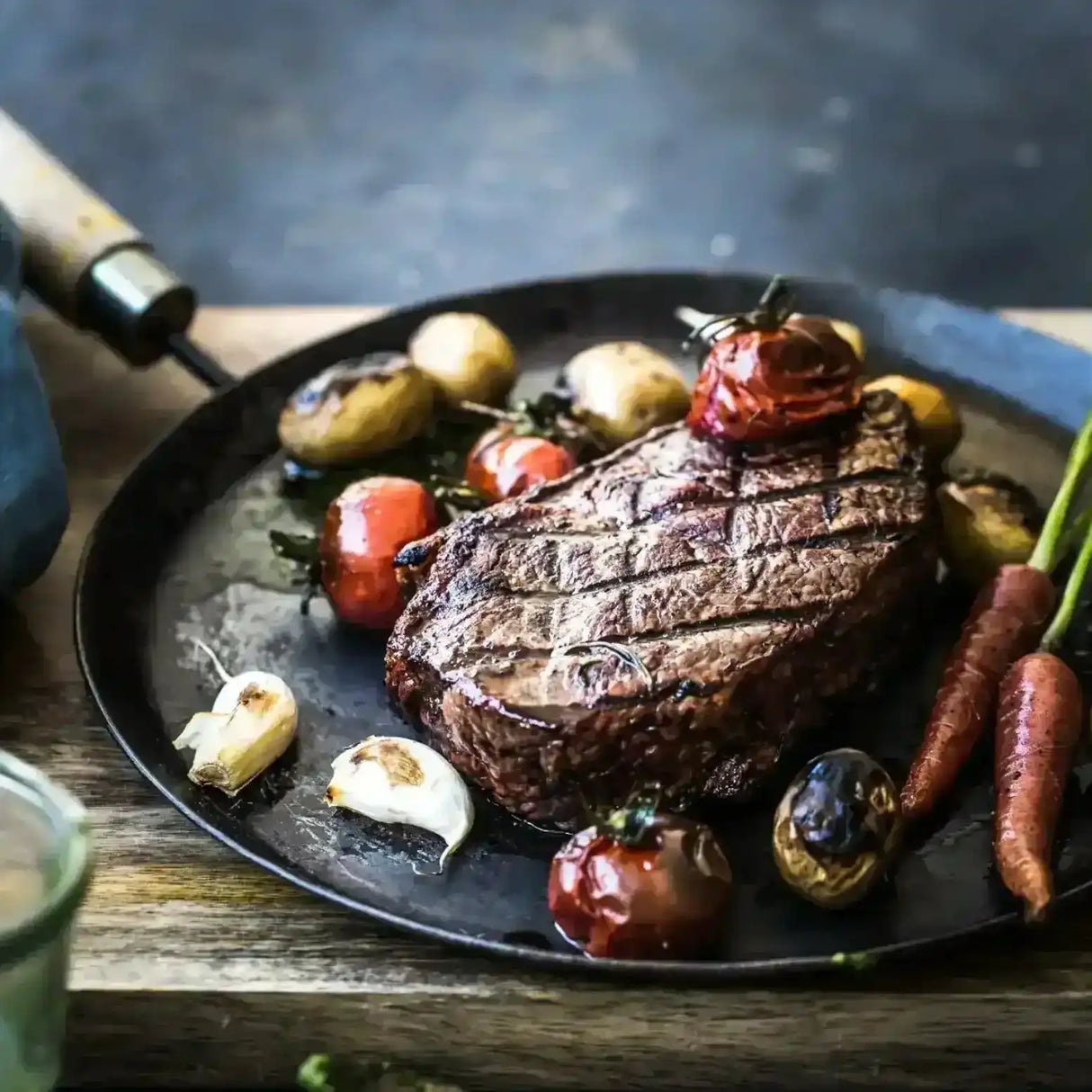 Cooked Wagyu sirloin steak with grilled vegetables, potatoes, tomatoes, carrots, and garlic on a plate.