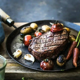 Cooked Wagyu sirloin steak with grilled vegetables, potatoes, tomatoes, carrots, and garlic on a plate.