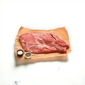Raw Angus brisket whole cut on butcher paper with dishes of salt and pepper on white background