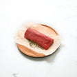 Raw Angus eye fillet log chateaubriand steak on parchment with fresh herbs on wooden board