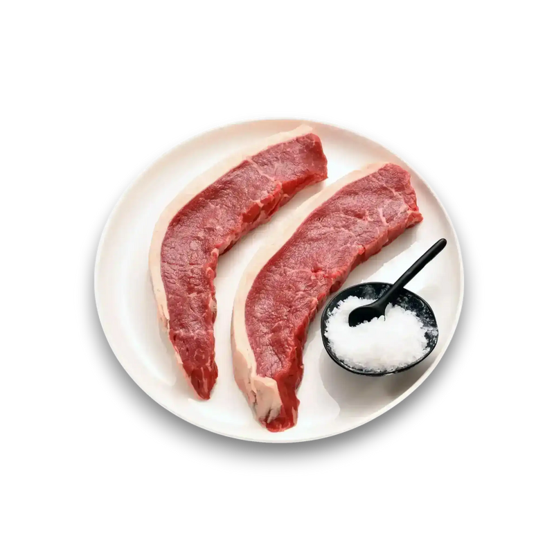 Two fresh raw beef steaks on white plate with coarse salt, premium grass-fed beef ready for cooking