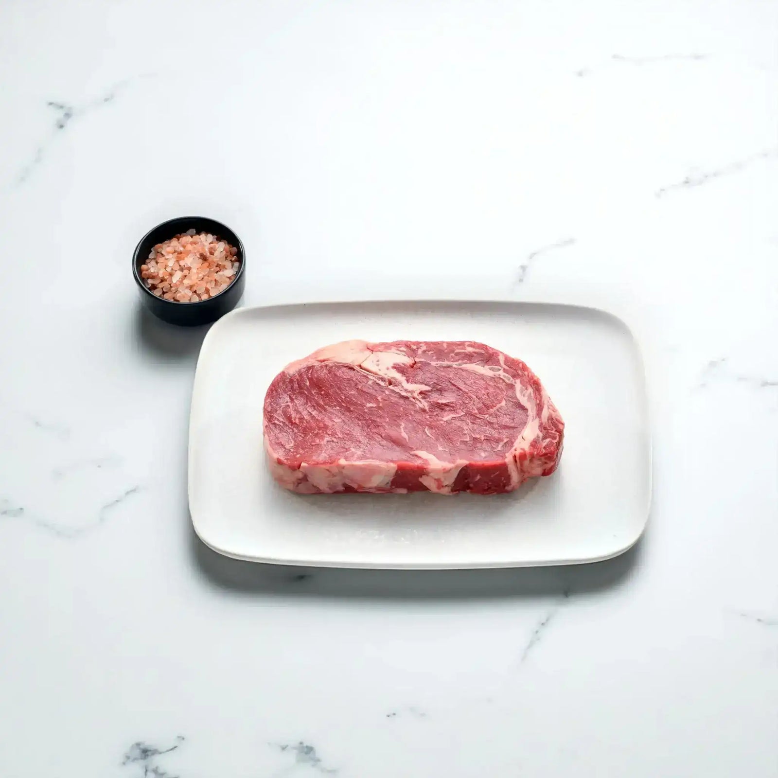 Angus rib fillet steak on a white plate with a bowl of pink Himalayan salt, Peter Augustus